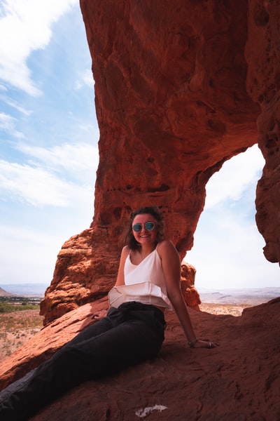白天，穿着白色背心和黑色裤子的女人坐在棕色岩石地层上